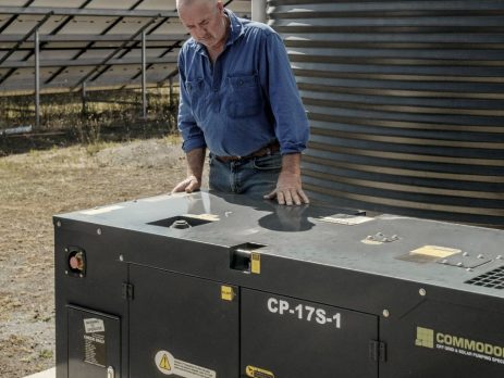 Man inspecting a Commodore diesel generator beside solar panels on a rural property